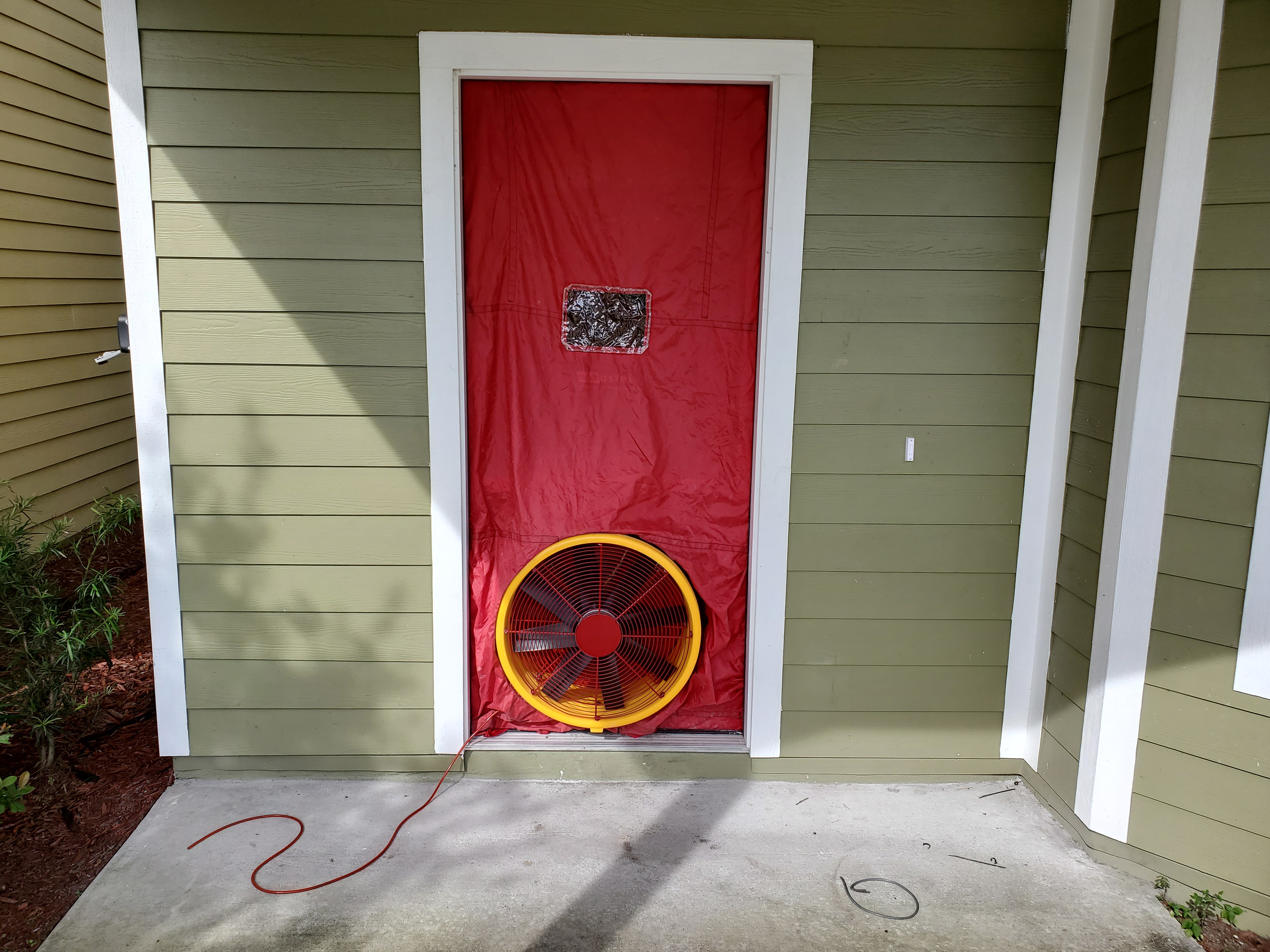 Blower door fan installed in exterior doorway of green-sided residential building