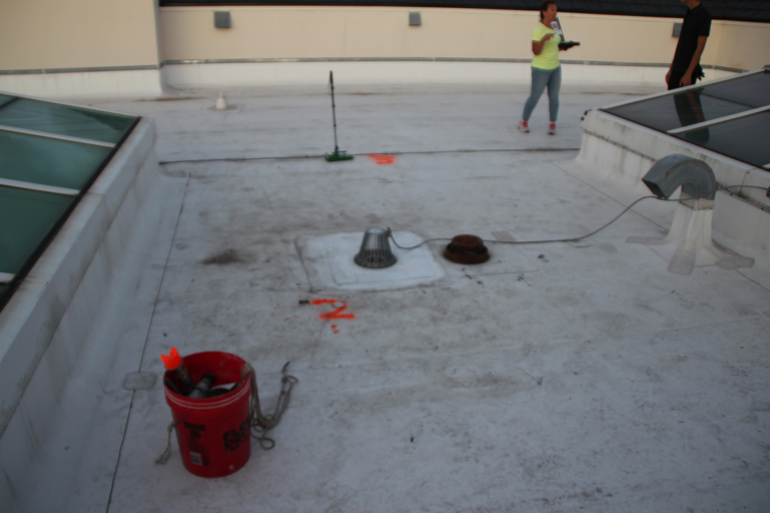 Flat roof with orange spray-paint IR survey marks and moisture testing crew